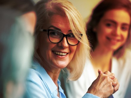 Smiling aged businesswoman looking listening to colleague at team meeting