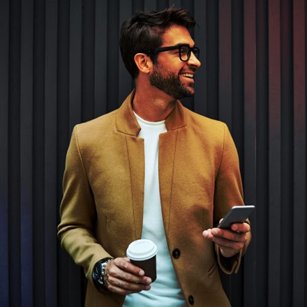 Smiling businessman with smart phone and cup.