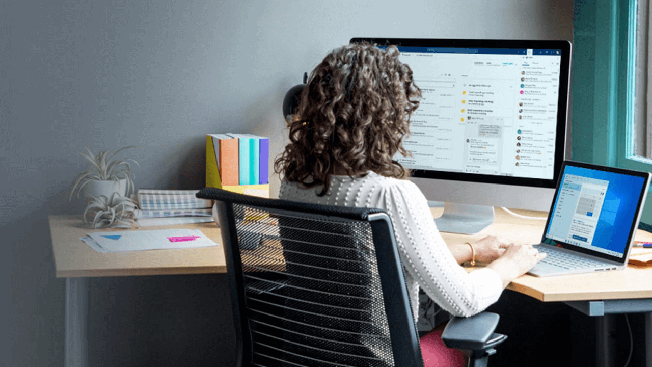 Curly haired woman working on a corner desk on two devices. 