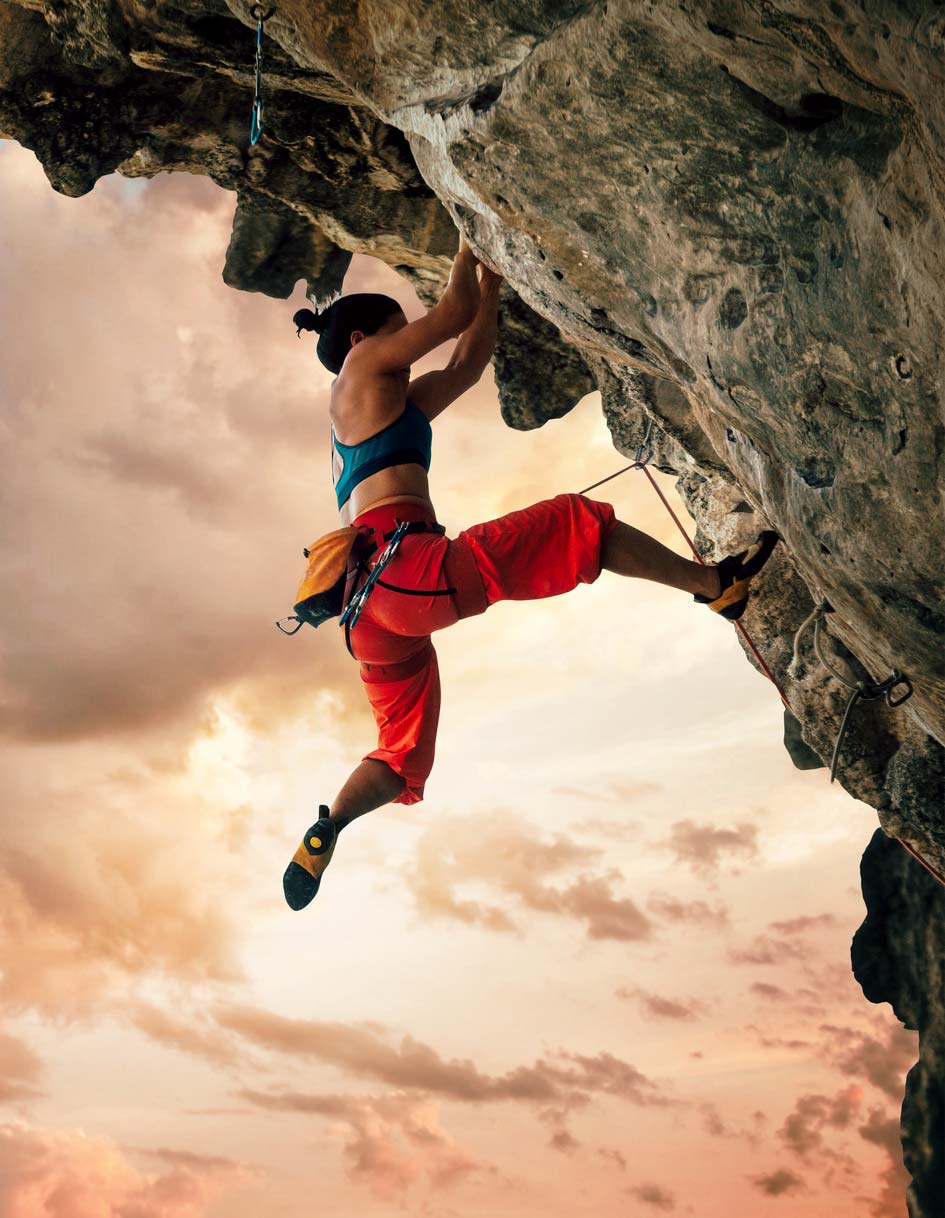 Athletic Woman climbing on overhanging cliff rock with sunset sky background