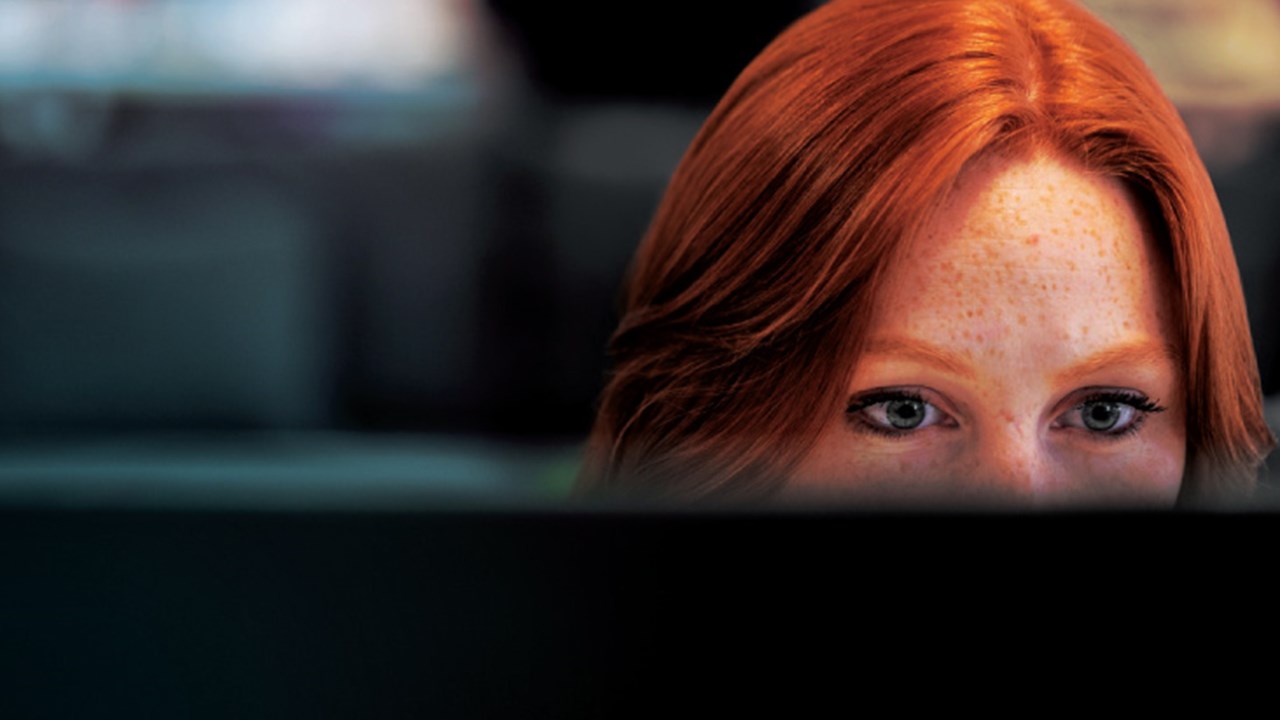 Red haired woman half hidden behind her screen at work. 