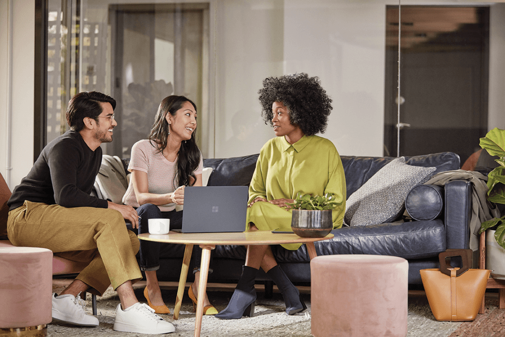 Three multi-cultural co-workers discussing a project, with a Microsoft Surface device on the table between them. 