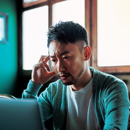 Asian man looking perplexed about his finances on a laptop screen